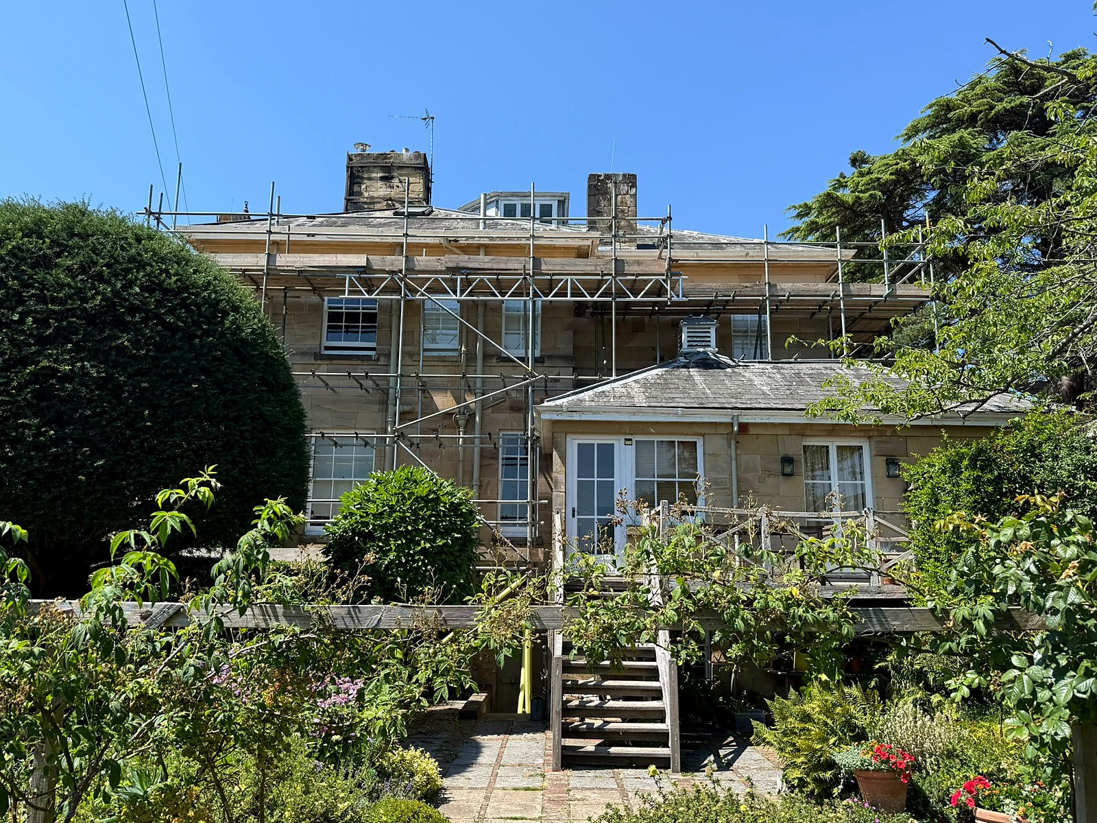 A period stone house under full-elevation scaffold, boarded to roof level